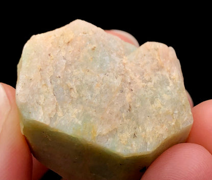 Close-up of a person holding The Crystalary's AUCTION- Amazonite, originating from Lake George, Park County, Colorado, USA. The stone displays a light greenish hue and textured surface, showcasing its vitreous luster against a dark background.