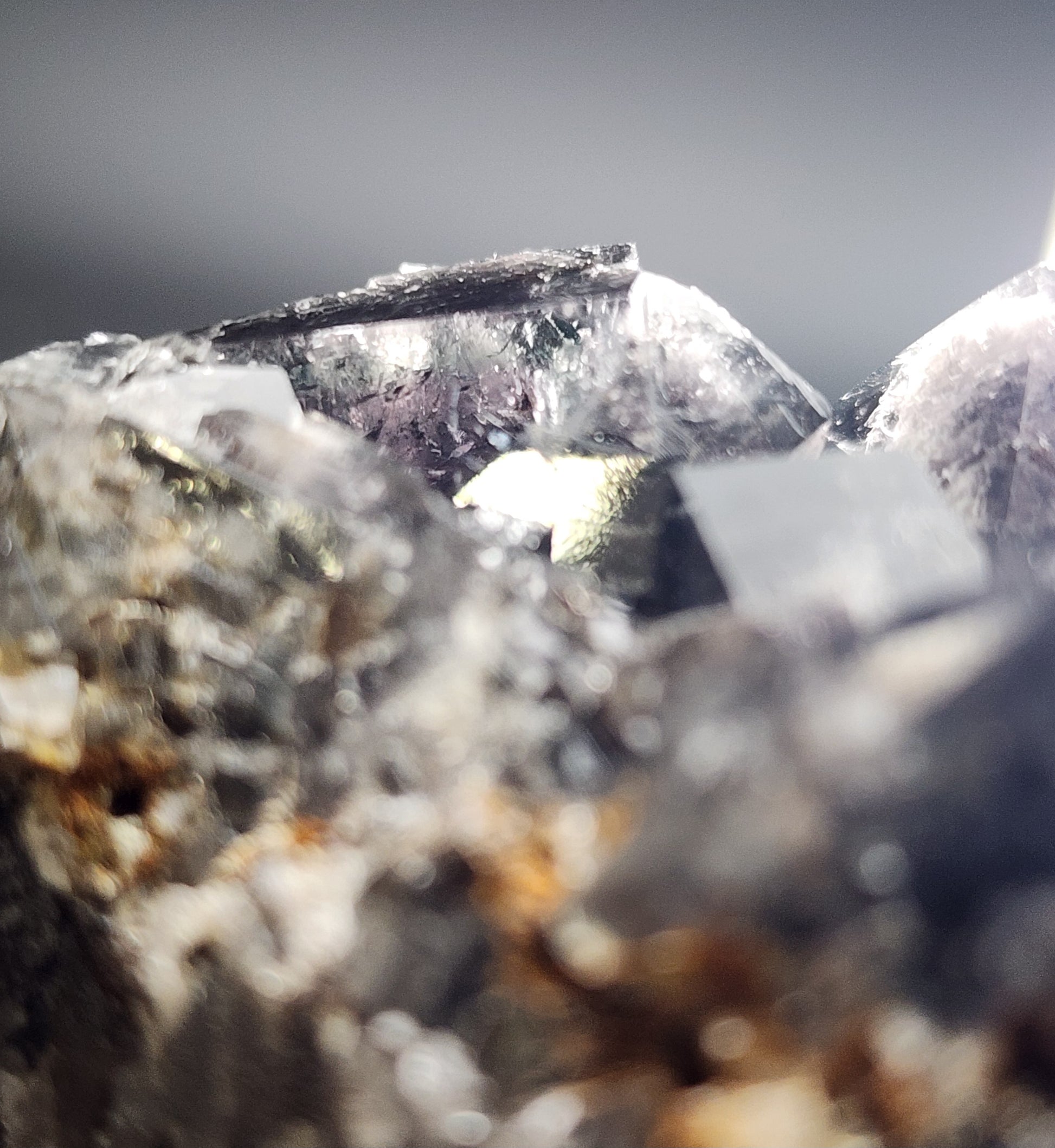 Close-up of a crystalline structure showcasing various sharp-edged, translucent crystals with a mix of dark and light reflections. This Fluorite - Yum Yum Pocket cluster image from Diana Maria Mine in Frosterley, Weardale, England features textured surfaces with a shiny, metallic appearance in some areas and diffused daylight fluorescence, enhancing the intricate details. Presented by The Crystalary.