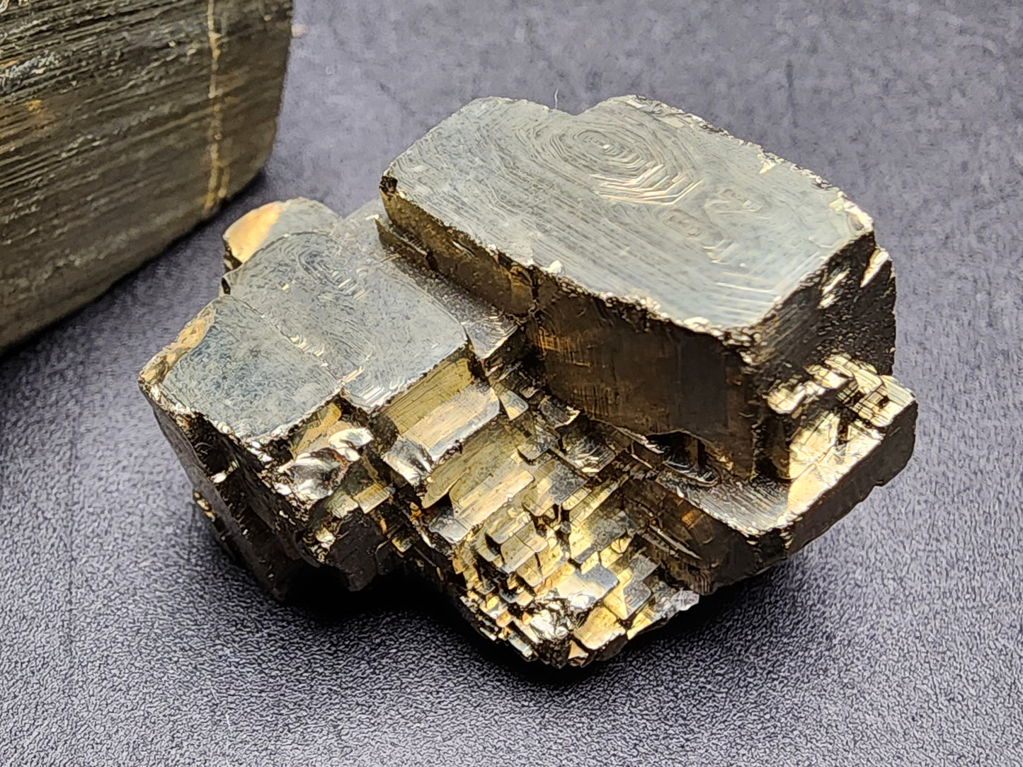 A stunning large, metallic pyrite cube from Ambas Aguas, Muro de Aguas, La Rioja, Spain is beautifully showcased against a dark background. This AUCTION Pyrite from The Crystalary boasts a magnificent golden-bronze luster with well-defined, striated surfaces and edges. It features an intricate, stacked formation that emphasizes its geometric crystalline structure—truly one of the finest pyrite specimens available.