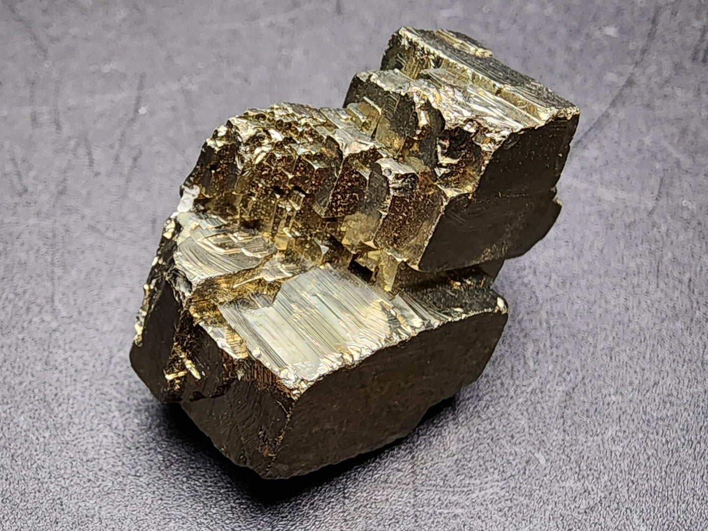 A shiny, metallic-looking mineral sample with a brassy yellow color and a reflective surface, characterized by jagged, uneven surfaces and striated textures, sits against a dark background. This crystalline structure with sharp, angular facets is one of The Crystalary's remarkable AUCTION Pyrite specimens from Ambas Aguas in La Rioja, Spain.