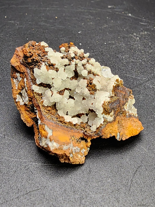 **The Crystalary's AUCTION Hemimorphite from the Ojuela Mine in Mapimi, Durango, Mexico showcases clusters of clear to white Hemimorphite crystals on a rough, brownish rock surface. Displayed against a dark background, the contrasting colors and textures emphasize the intricate crystalline details.**