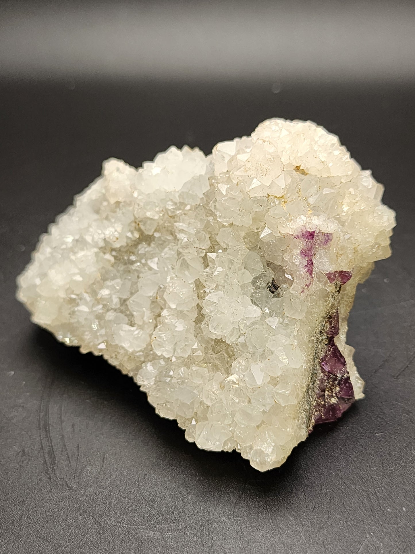 A close-up image showcases a cluster of clear and sparkly Quartz over Fluorite from The Crystalary, with irregularly shaped crystals and small patches of purple fluorite, originating from an unknown Chinese locality.