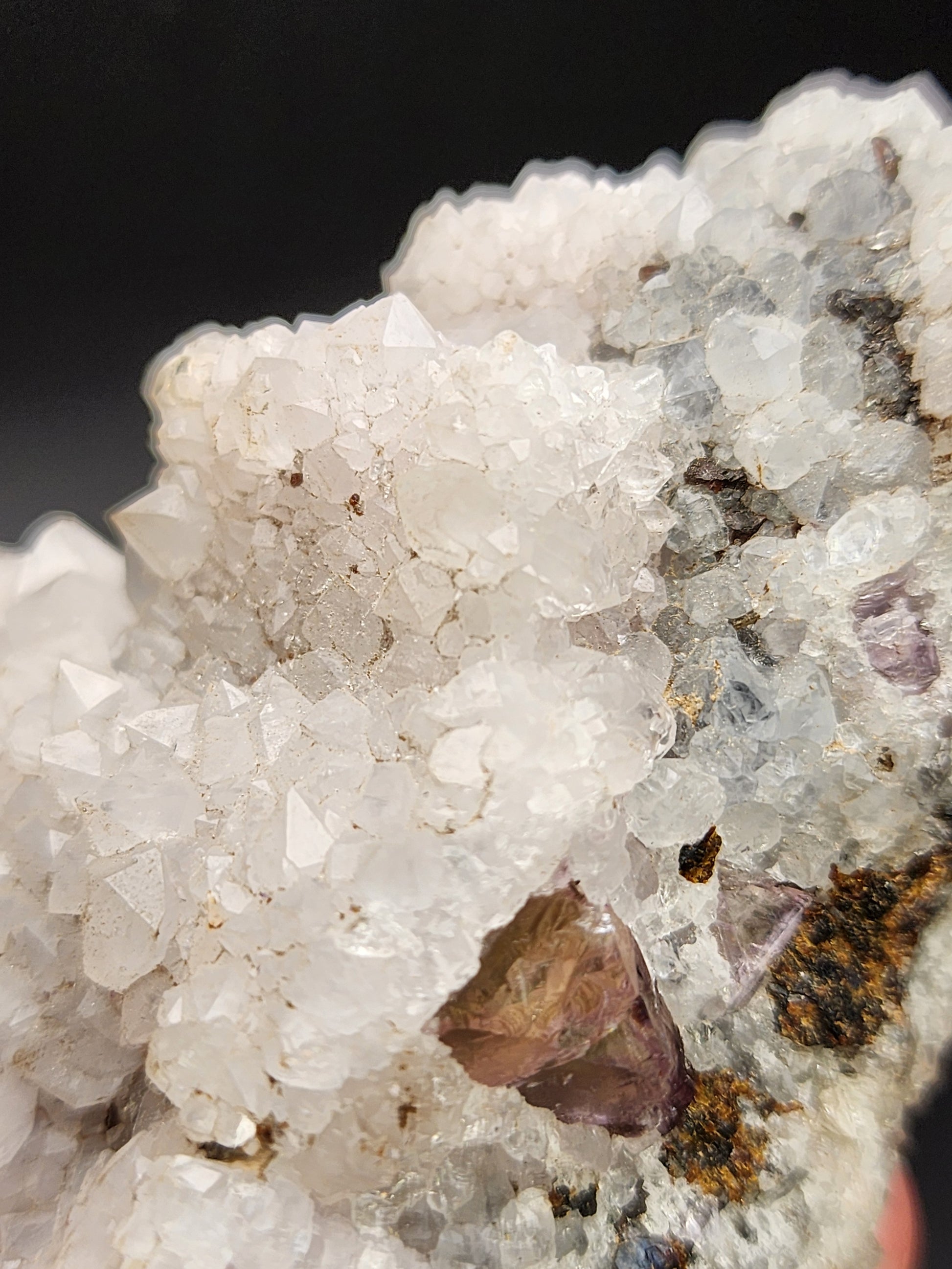 Presenting the AUCTION Quartz over Fluorite from an unknown Chinese locality by The Crystalary: a close-up view of this mineral specimen reveals numerous small, pointed translucent fluorite crystals on its surface. Sparkly white quartz is densely clustered together, with patches of brown and purple minerals interspersed among them, all set against a dark background.