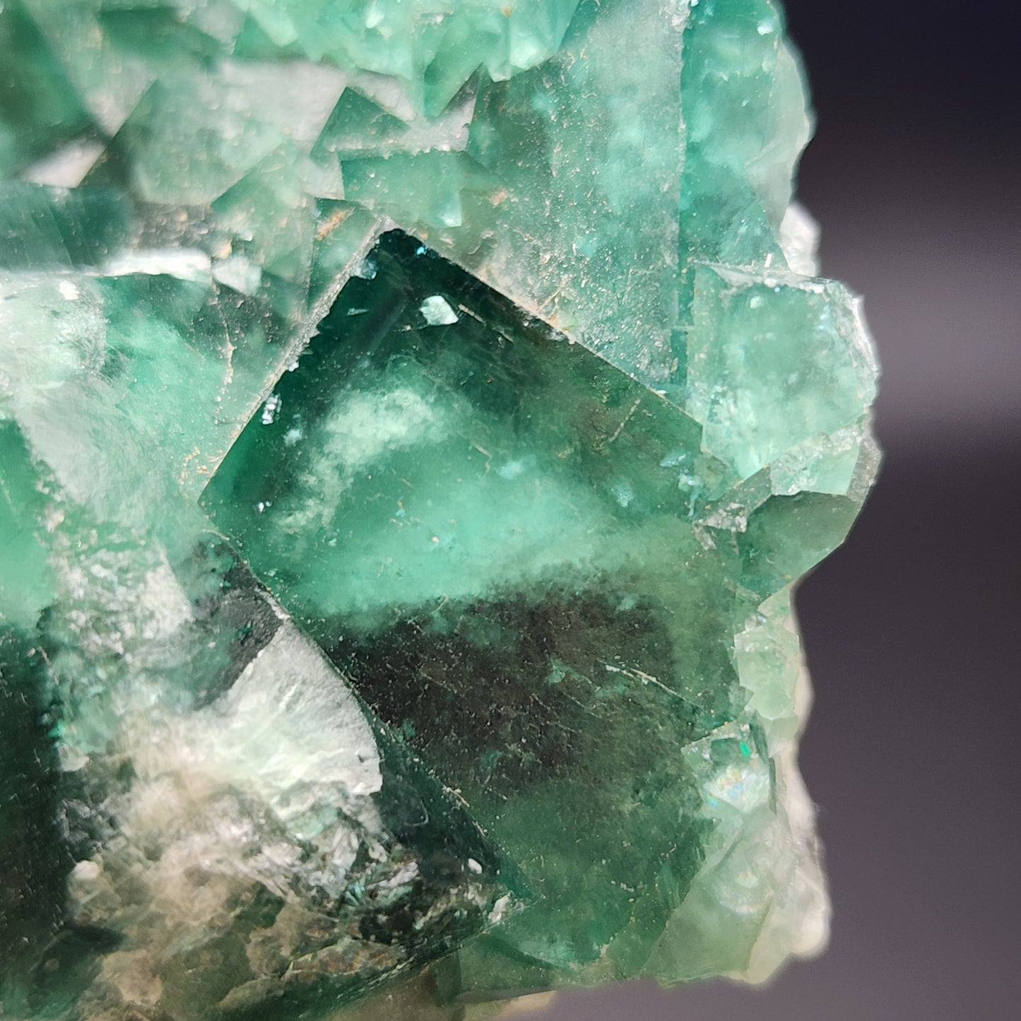 Close-up image of The Crystalary's raw green fluorite crystal cluster, sourced from the Fluorite Occurence in Mandrosonoro, Ambatofinandrahana, Amoroni'i Mania, Madagascar. The cluster showcases visible cubic formations with varying shades of green and translucent areas, highlighting its natural facets and edges against a dark background.