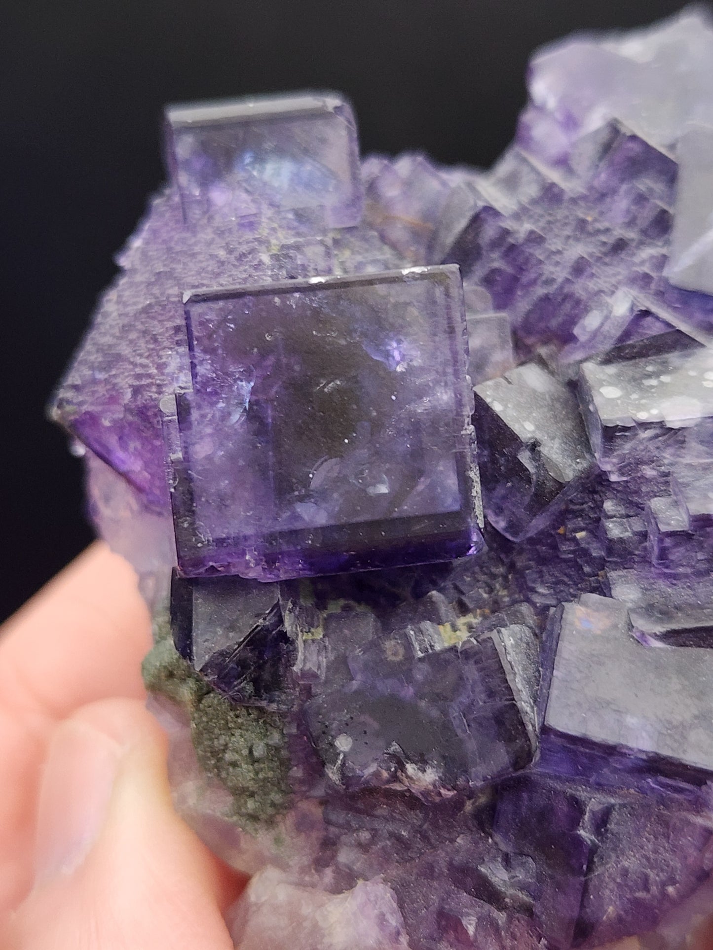 Close-up of a hand holding a medium cluster of high luster cubes from The Crystalary's Fluorite collection, sourced from Larkin's Quarry, Shannapheasteen, Costelloe, Connemara, Galway County. The translucent purple cubic fluorite crystals reveal intricate geometric shapes and various shades of purple.