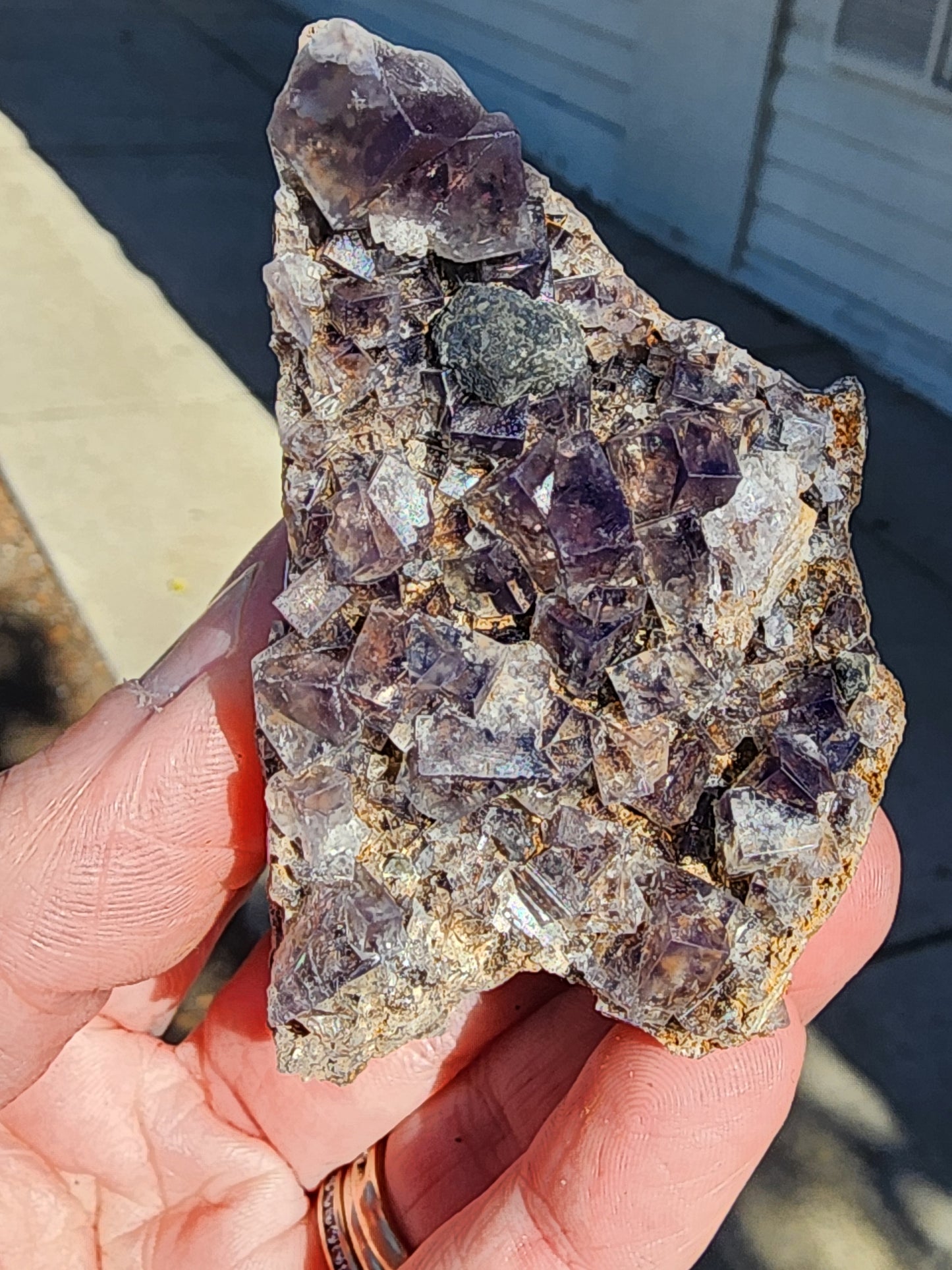 A person carefully holds a Fluorite - Smoky Rabbit Pocket from The Crystalary, sourced from the Diana Maria Mine in Frosterley, Weardale, Co. Durham, England (sku3014), admiring its natural beauty.