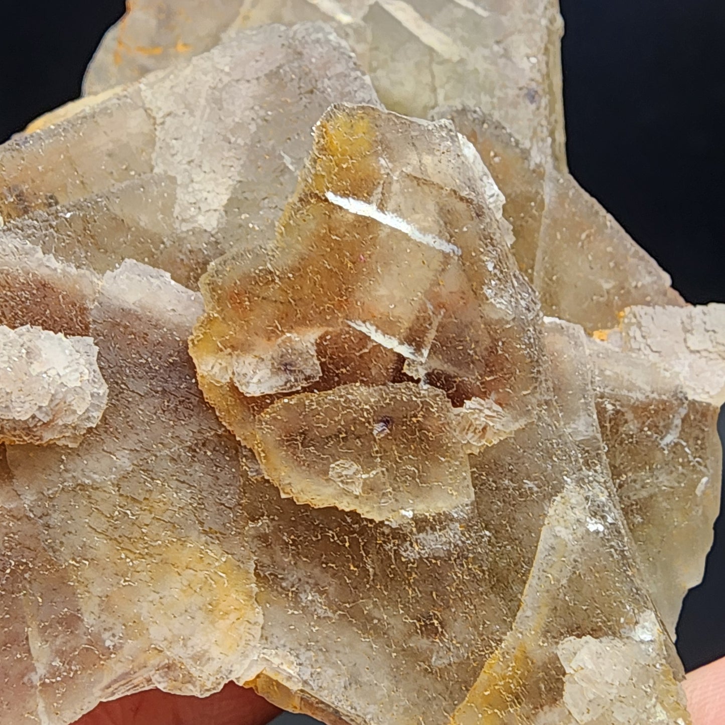 A person holds a cluster of The Crystalary's "Fluorite - Heißer Stein Mine" specimen, featuring translucent crystalline structures with irregular shapes and earthy tones, from light brown to pale yellow. This piece has a rough texture and layered appearance, reminiscent of the treasures found in Heißer Stein Mine (SKU 3080).