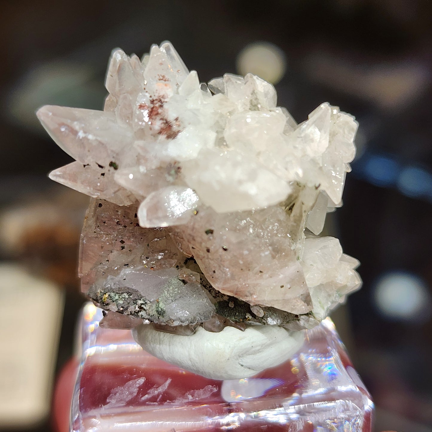 Close-up of Quartz v. Amethyst with calcite from Tonglushan Mine, featuring sharp formations on a small base. The slightly cloudy crystals show hints of pink and green inclusions, enhanced by calcite traces, elegantly displayed on a clear stand. Available from The Crystalary, SKU 3101.