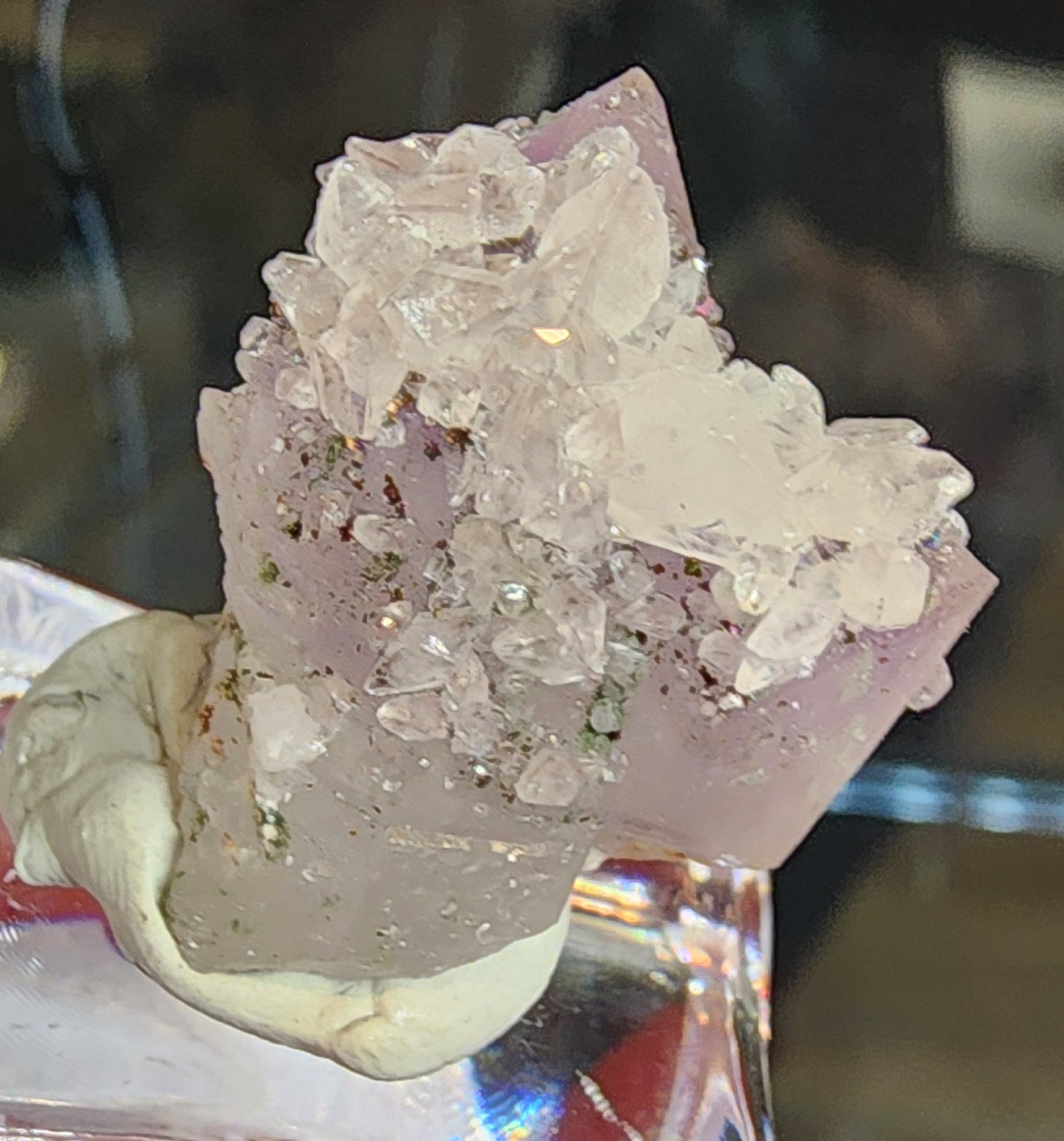 A close-up of The Crystalary's Quartz v. Amethyst, Calcite (sku 3102) from Tonglushan Mine displays pink and clear crystals on modeling clay atop a clear acrylic stand, with a dark background accentuating its dazzling features.