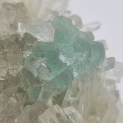 A close-up of The Crystalary's Fluorite with Quartz SKU 801 from Huayllapon Mine, Peru shows a minty green cluster with clear facets. Light shimmers off the surfaces, while a softly blurred background highlights the intricate crystalline structures in their matrix.