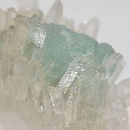 A detailed view of The Crystalary's Fluorite with Quartz (sku 801) from Huayllapon Mine, Peru, showcases mint green fluorite within clear quartz crystals. The translucent sharpness captures light beautifully against a softly blurred background.