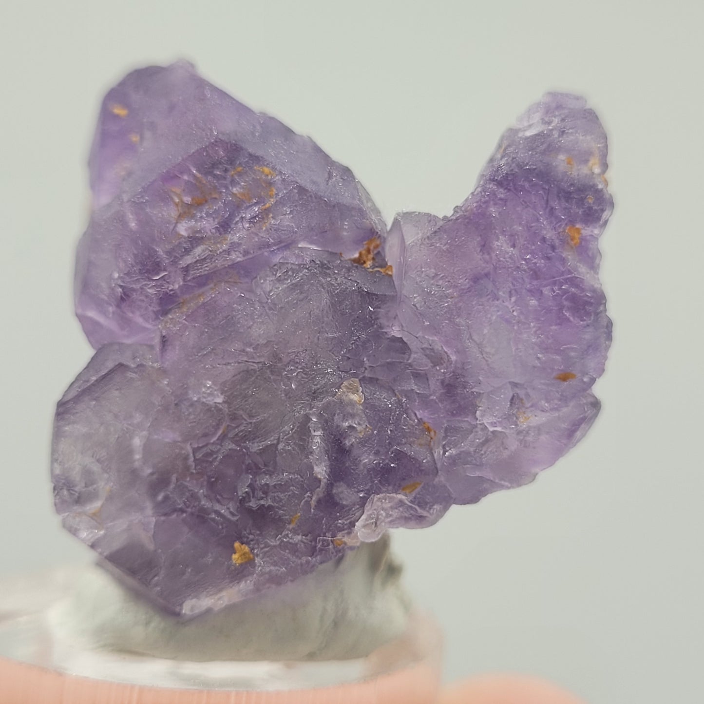 A close-up of the Fluorite- Huallanca, Ancash, Peru (sku 803) from The Crystalary shows a raw purple crystalline mineral cluster on an acrylic base, reminiscent of a refined specimen. It's set against a plain light grey background for emphasis.