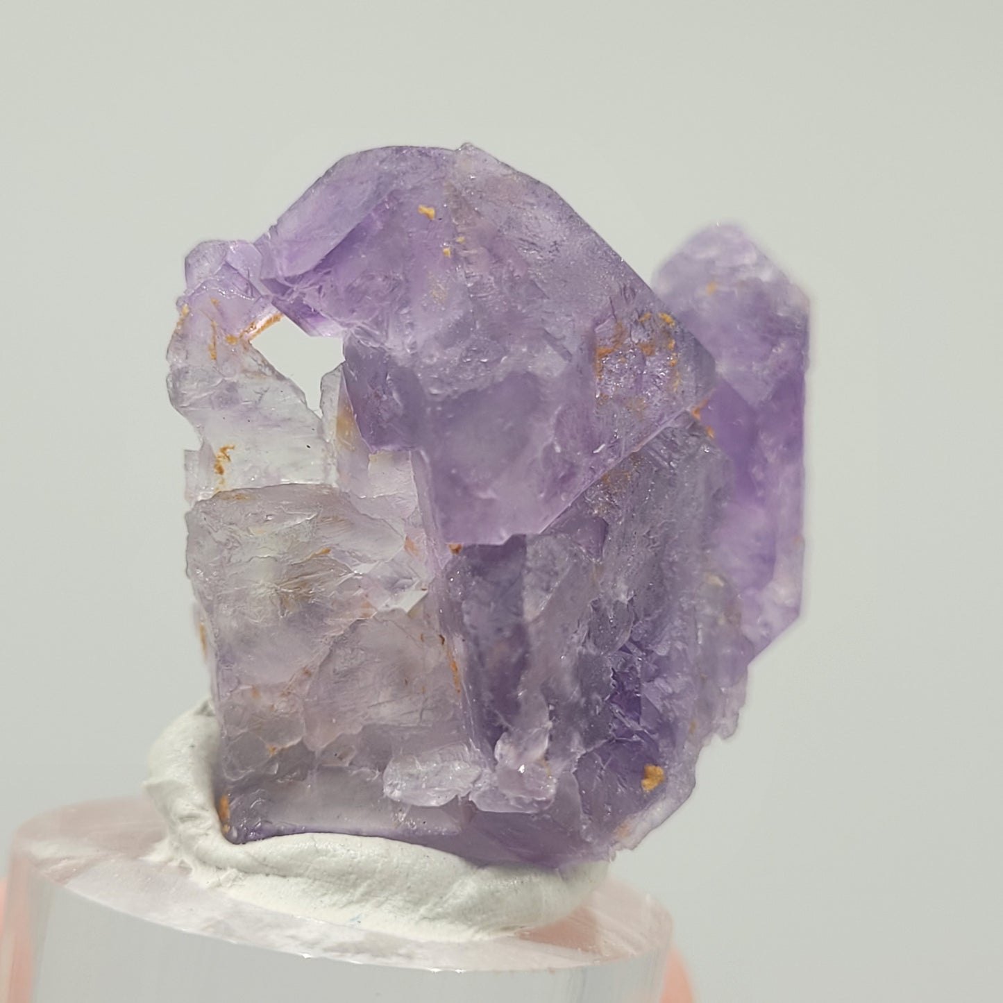 The Crystalary presents the Fluorite (Huallanca, Ancash, Peru, sku 803); a translucent purple specimen with jagged surfaces and subtle yellow inclusions on a sleek acrylic base, set against a light gray background.