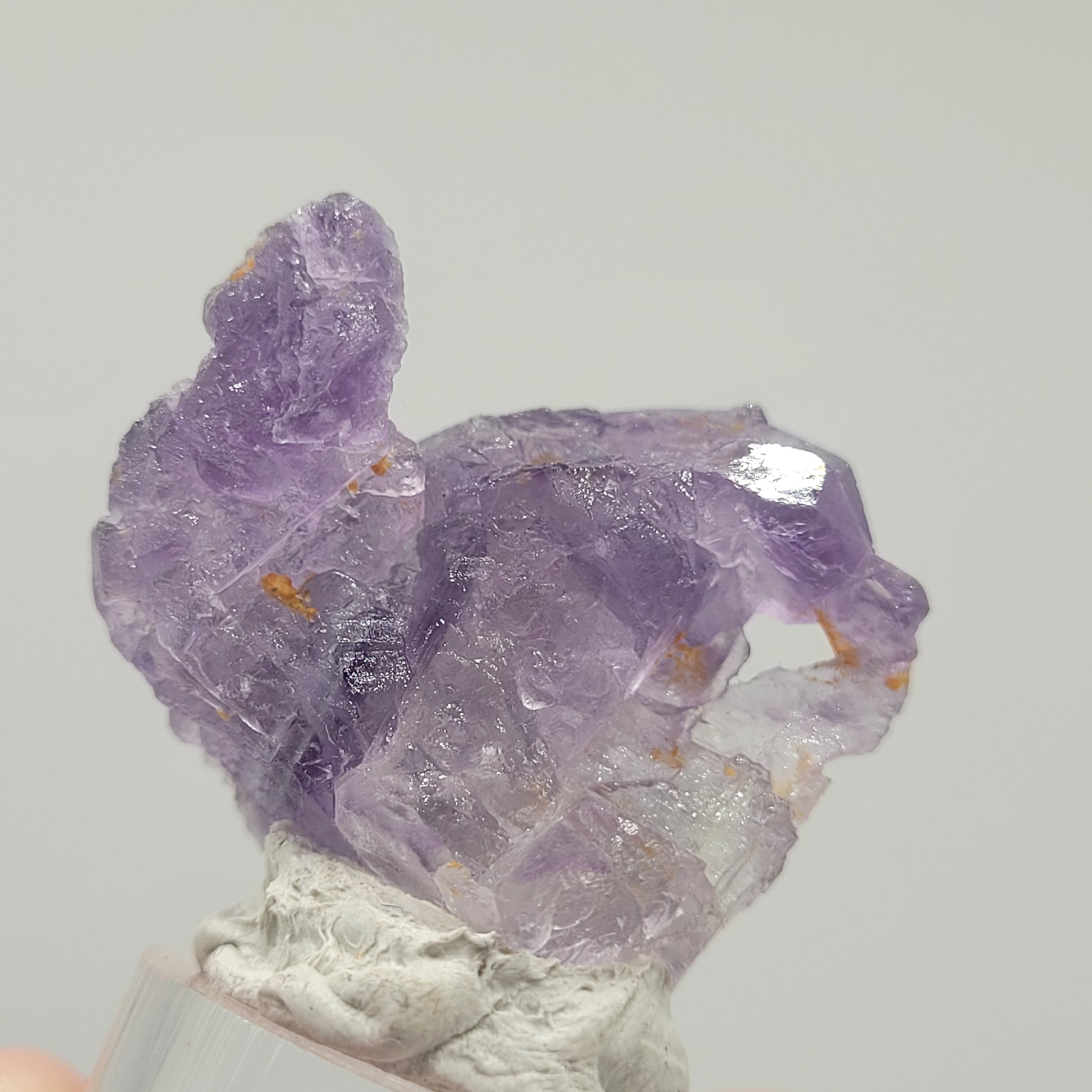 A purple fluorite specimen from Huallanca, Ancash, Peru (sku 803) by The Crystalary, features translucent and jagged edges. It sits on a small acrylic base against a plain gray background.