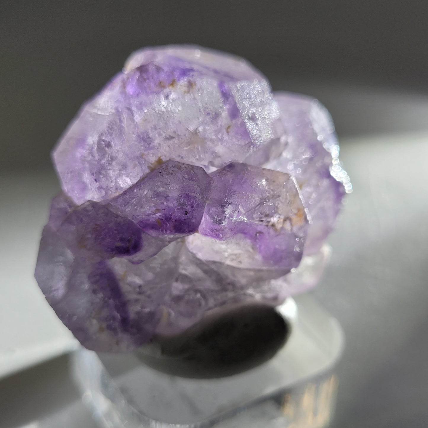 A close-up image of The Crystalary's Fluorite (Huallanca, Ancash, Peru, SKU 804) rests on a reflective surface, showcasing its irregular shapes and translucent facets highlighted by light.