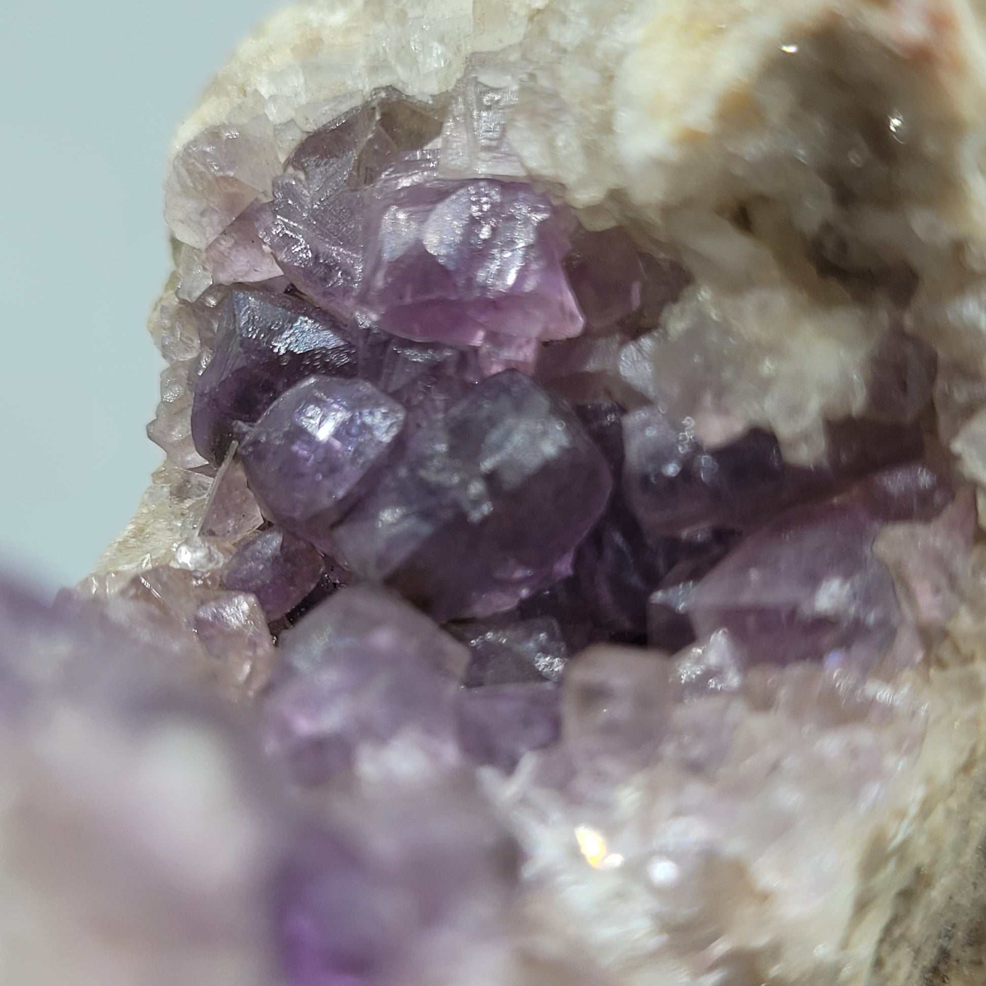 Close-up image of Fluorite crystals from the Jaimina Mine, Asturias, Spain. The specimen by The Crystalary showcases translucent crystals in varying purple hues set against a rough, pale rock surface. SKU: 810.