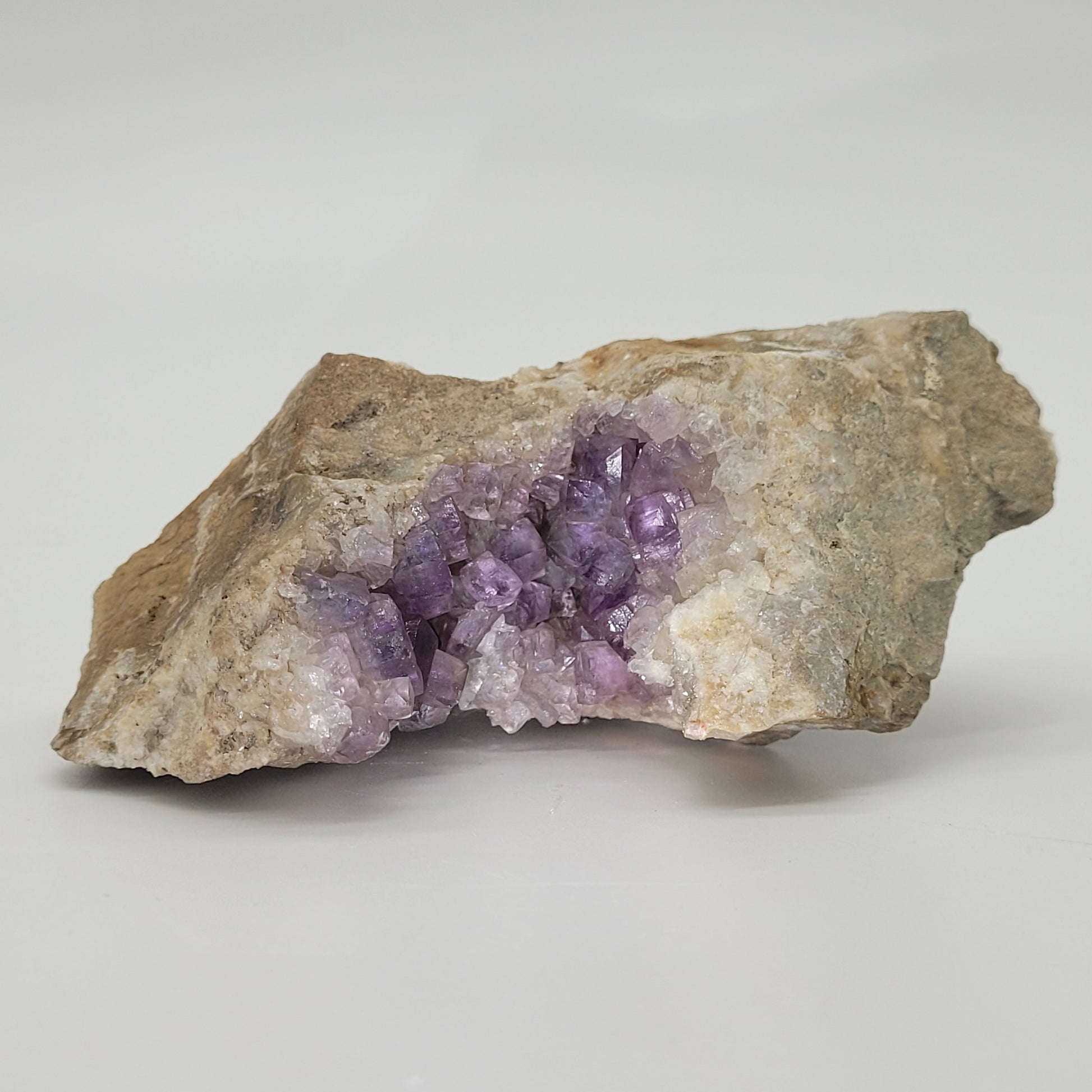 Fluorite from The Crystalary, SKU 810, showcases glossy crystals of various sizes on a pale base. Revealing its Spanish origins at the Jaimina Mine, these intricate clusters rest against a plain white backdrop.