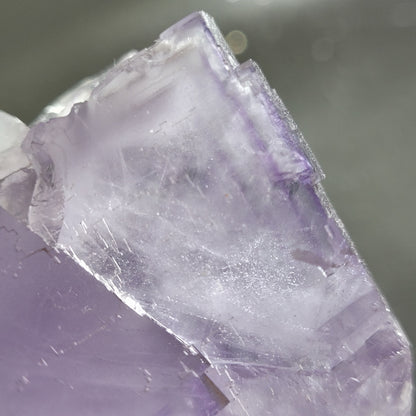 Close-up of a translucent, purple fluorite crystal from The Crystalary's Berbes collection (SKU 811), found in Ribadesella, Asturias, Spain. The rough edges and varied hues reflect light for a shimmering effect.