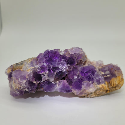 On a light surface rests Fluorite from Berbes, Ribadesella, Asturias (sku 812) by The Crystalary. Its vibrant purple hues with rough, jagged edges and blend of translucent and opaque sections reflect light beautifully.