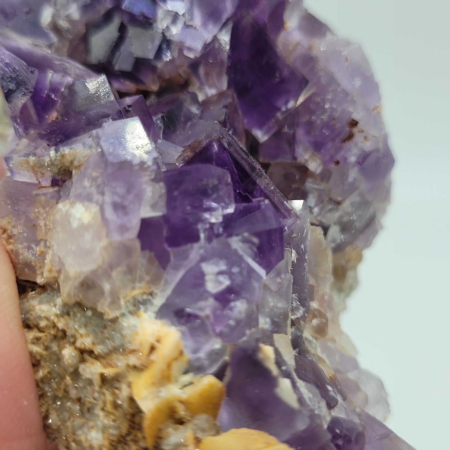 A close-up of a rough, purple amethyst crystal with violet hues and beige mineral hints mirrors the stunning Fluorite from Berbes, Ribadesella by The Crystalary. Its jagged facets create a textured appearance against a light backdrop. (SKU 812).