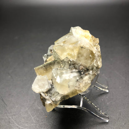 A large, translucent fluorite crystal from The Crystalary, sourced from The Bull Vein at the Lady Annabella Mine in Eastgate, Weardale, Co. Durham, England, rests on a clear plastic stand against a dark background. Its pale yellow and clear jagged surfaces reflect light beautifully, showcasing its natural formation akin to the stunning finds from this renowned mine.