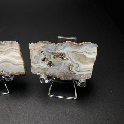 A close-up of The Crystalary's AUCTION- Agate from Fourth of July Peak (Fourth of July Butte), Hassayampa, Maricopa County, Arizona, USA is displayed on a clear stand against a black background. The agate showcases swirling patterns in shades of white, gray, and brown, with a central cloudy feature reminiscent of textures found near Fourth of July Peak.