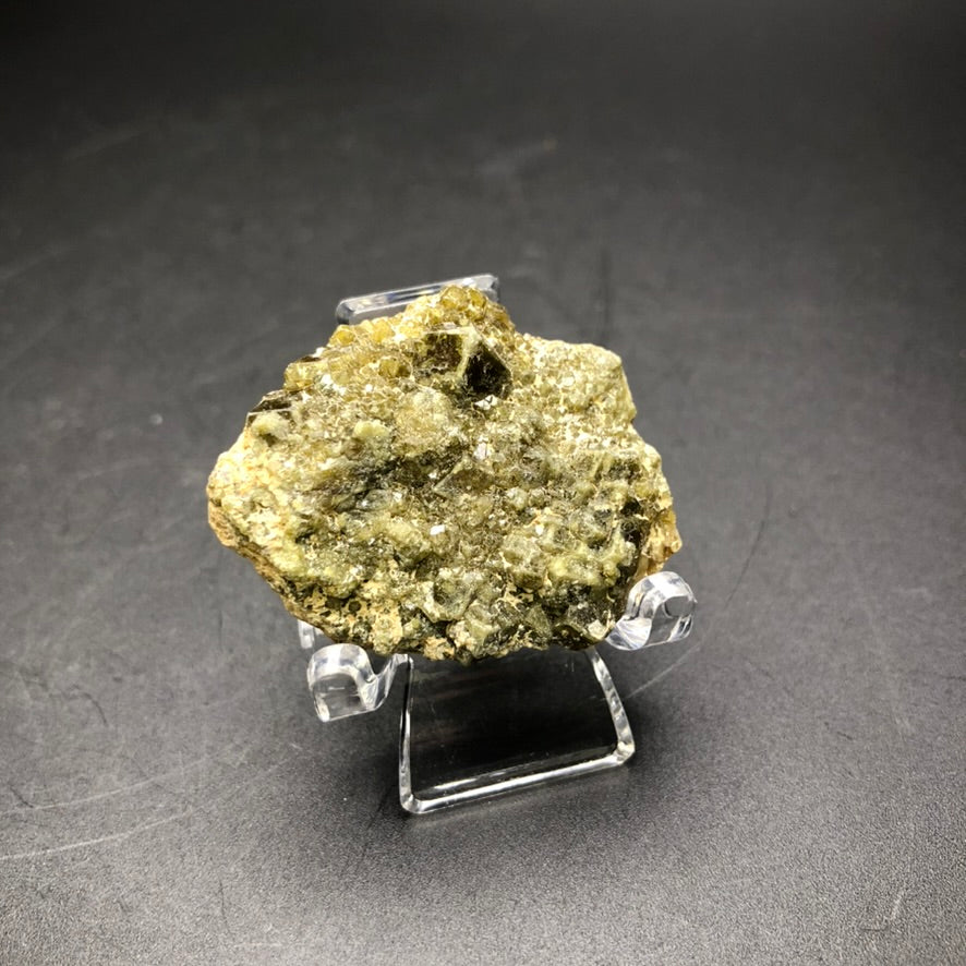 Displayed on a clear stand against a dark background is an AUCTION- Dermantoid Garnet specimen from Tubissis, Erongo, Namibia, by The Crystalary.