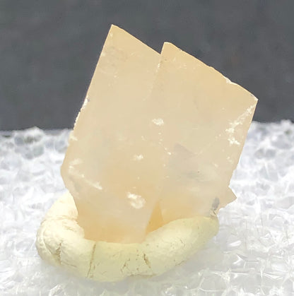 The Crystalary's AUCTION- Calcite from Otero County, Colorado, USA showcases two stacked rectangular formations of translucent honey calcite elegantly resting on a white textured surface and light clay base.