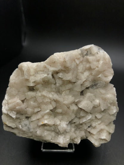 A detailed shot of a rough, white mineral rock from The Crystalary's AUCTION-Dolomite, Calcite collection, showcasing clear dolomite crystals with distinctive formations against a dark backdrop. The texture is granular and uneven, with subtle hints of gray. Origin: Thunder Bay, Ontario, Canada.