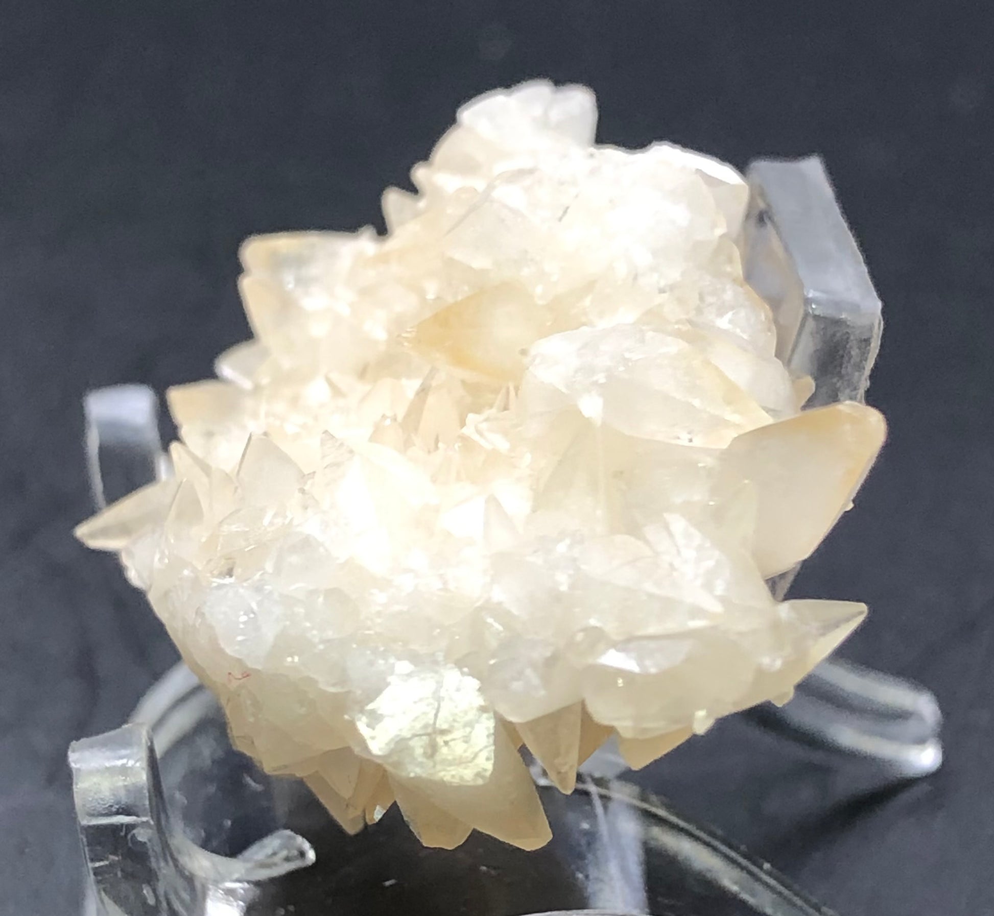 A close-up shot of The Crystalary's translucent peach calcite cluster from Southwest Mine, Hendricks Gulch, Bisbee, Cochise County, Arizona. Set on a clear stand against a dark background, these crystals exhibit a slightly glossy finish with natural jagged shapes and fine details.