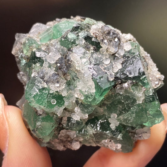 A close-up view of a hand holding a cluster of green and clear minerals from the Diana Maria Mine. The specimen showcases a beautiful crystalline structure with vibrant green and translucent white areas, identified as Fluorite from the Northern Lights Pocket in Co. Durham, England by The Crystalary.