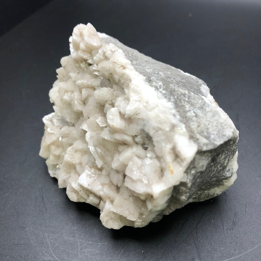 A rugged specimen from The Crystalary, featuring AUCTION- Dolomite and Calcite sourced from Thunder Bay, Ontario, Canada, displays a multitude of white angular crystals coupled with light pink calcite formations against a dark background.