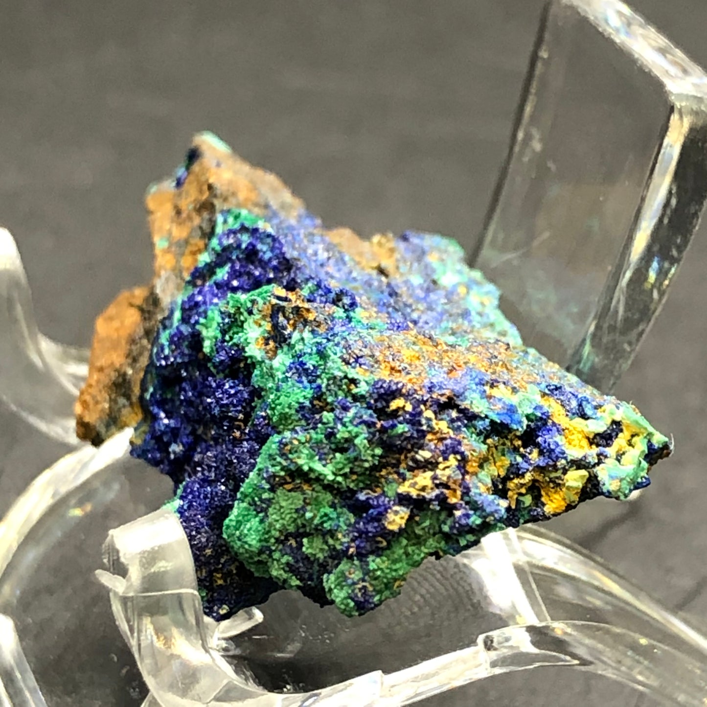 A close-up of "AUCTION- Azurite Malachite- Bisbee, Conchise County, Arizona, USA" by The Crystalary shows vibrant deep blue druzy azurite and green malachite with brown and yellow spots. This mineral is displayed on a transparent stand against a dark background, echoing the treasures from Bisbee.