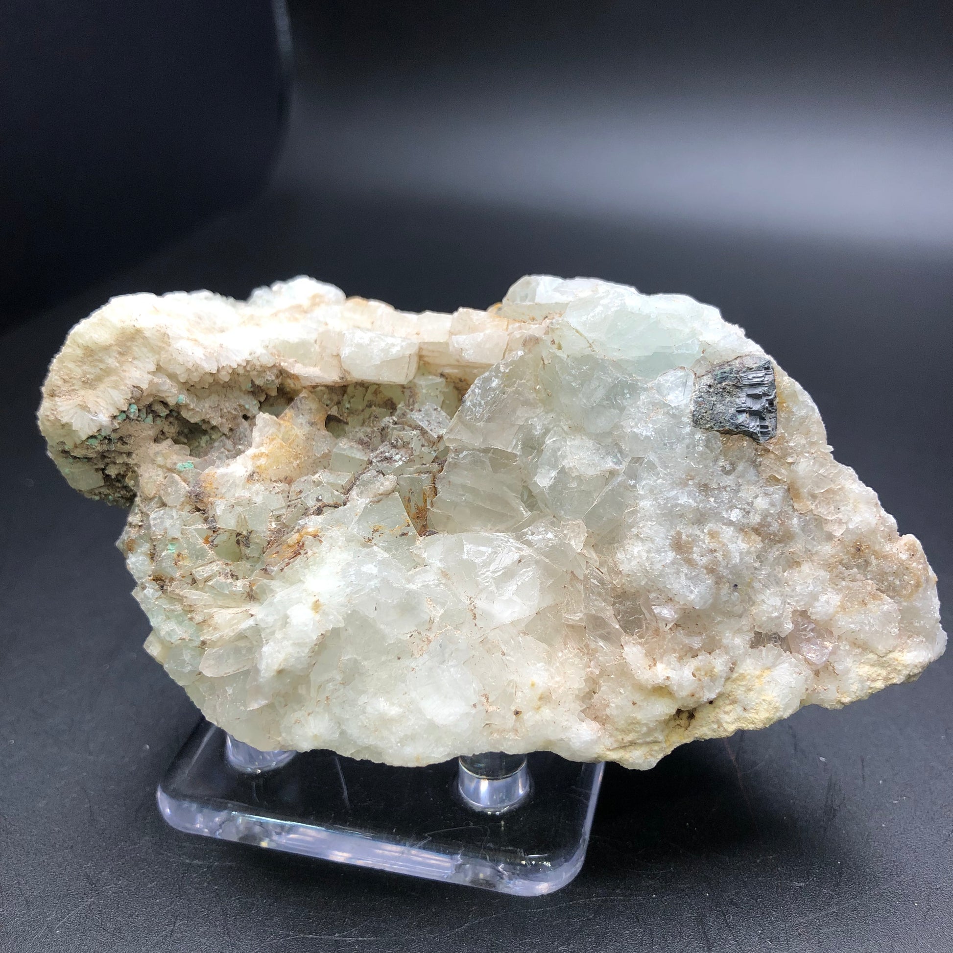 A rough mineral specimen from The Crystalary's AUCTION- Calcite, Quartz collection boasts translucent and opaque crystal formations in shades of white, beige, and pale green with hints of light blue calcite, elegantly displayed on a clear stand against a black background.