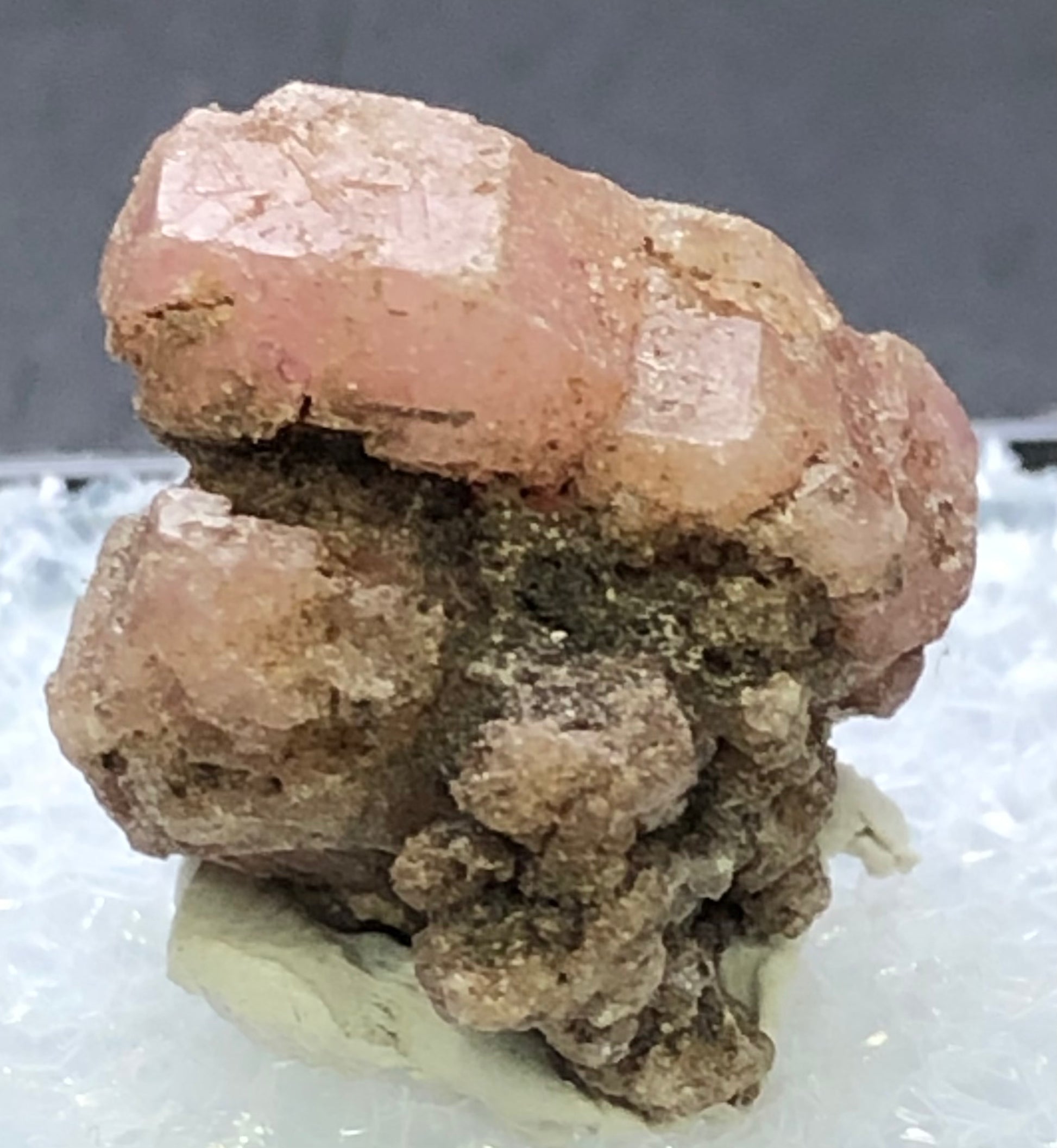 The Crystalary's AUCTION - Garnet, Grossular from Morelos, Mexico features a rough pink-brown crystalline structure on a small white base against a soft black background, reminiscent of dusty rose pink garnet.