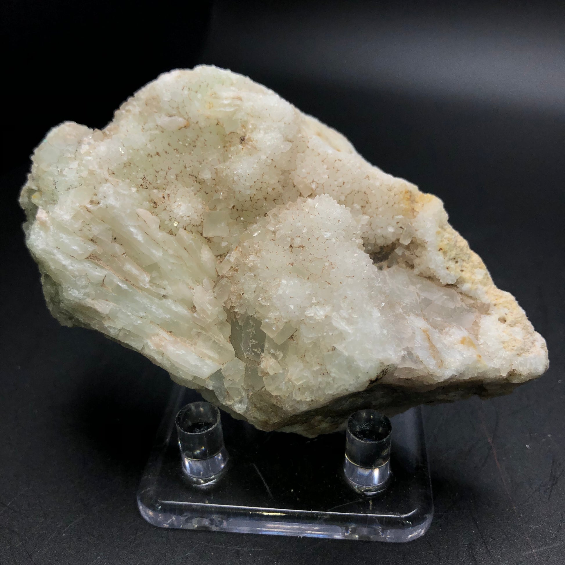 A large, irregularly shaped mineral from The Crystalary's AUCTION: Calcite, Quartz collection showcases crystalline formations on a clear stand set against a black background. Its surface glistens with a coarse, shimmering texture.