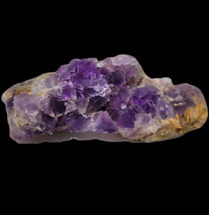 A raw purple amethyst crystal with jagged edges and visible layers sits on a plain black background, showcasing its vibrant color and natural texture, reminiscent of The Crystalary's Fluorite - Berbes from Ribadesella, Spain (SKU 812).