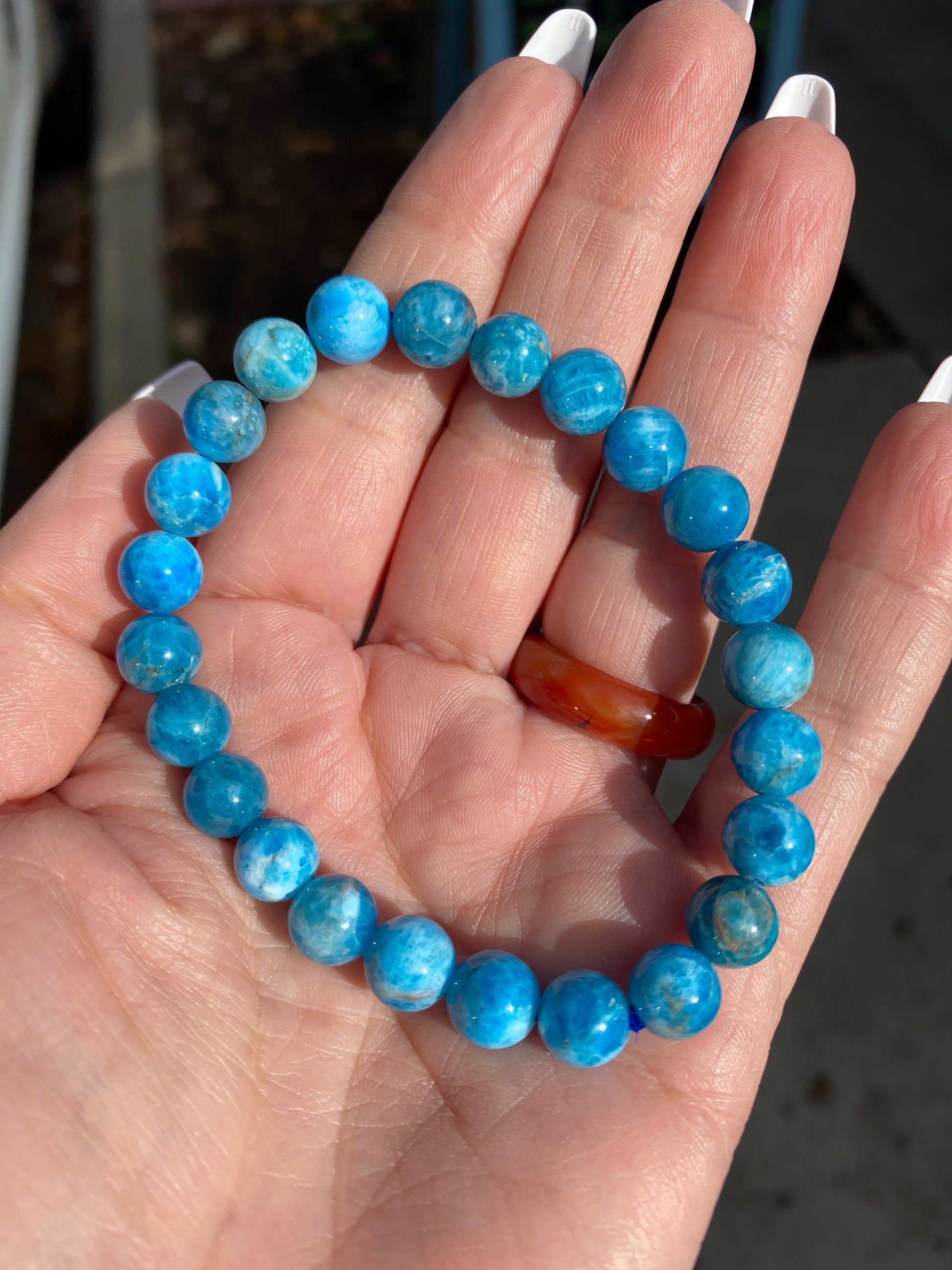 A hand displays The Crystalary's Blue Friendship Bracelet, its radiant 8mm Blue Apatite beads shimmering in the sunlight and enhancing their glossy allure.