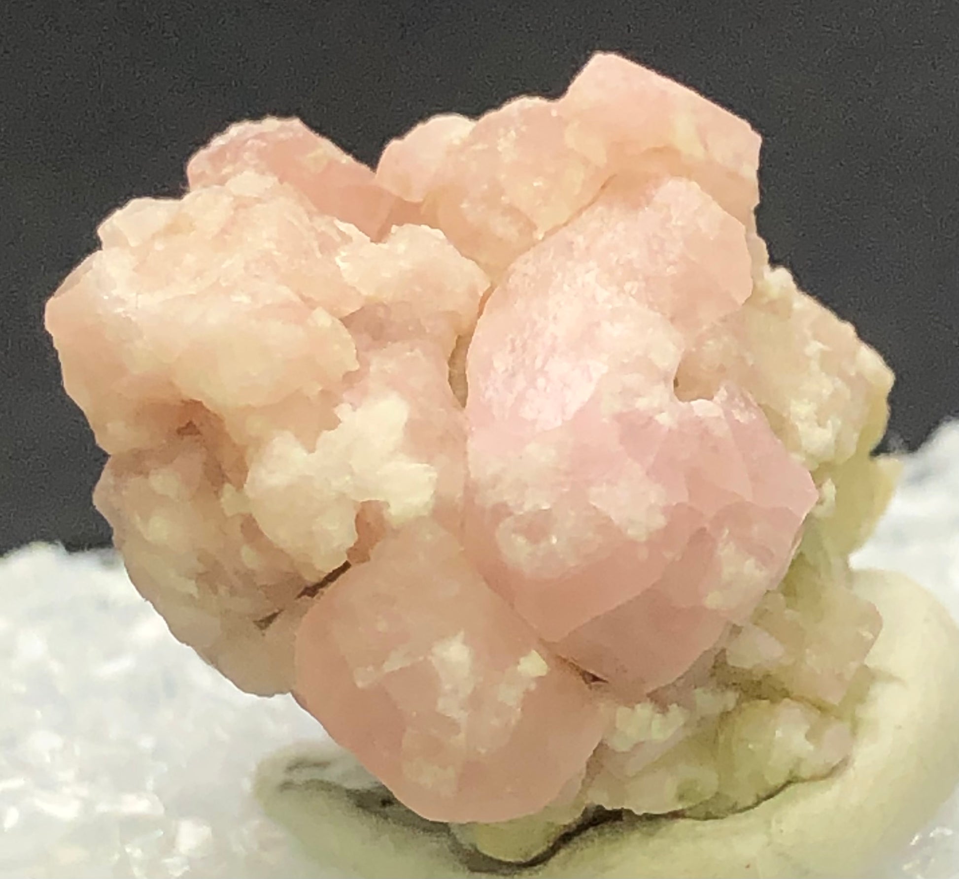 Close-up of Grossular Garnet crystals from Morelos, Mexico, by The Crystalary. These light pink minerals feature a rough surface against a blurred dark background and possess a soft, delicate, slightly translucent appearance.