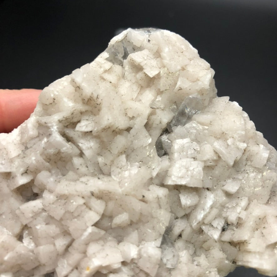 The Crystalary's AUCTION- Dolomite, Calcite mineral cluster from Thunder Bay, Ontario is showcased against a plain black background, with a close-up focus on a hand holding this captivating piece featuring white crystalline formations embedded with light pink calcite and clear dolomite crystals.