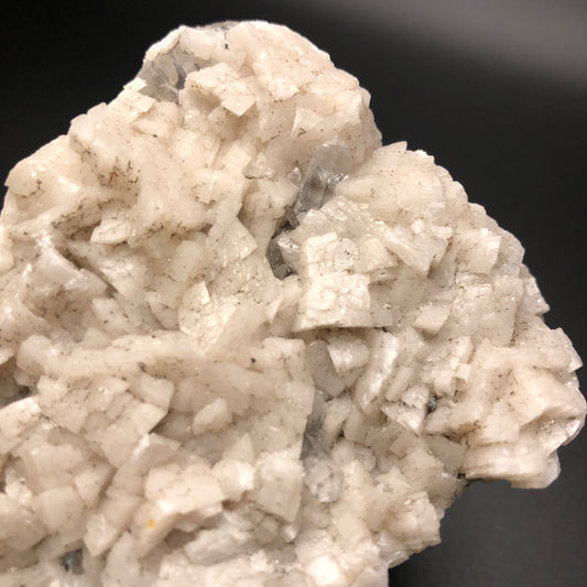 Close-up of a mineral specimen highlighting Dolomite & Calcite from Thunder Bay, Ontario, Canada. The crystals exhibit a cluster of small, white, blocky shapes against a black background. The texture is rough with evident natural imperfections, featuring an array of angles and surfaces reminiscent of those found in The Crystalary's collection.