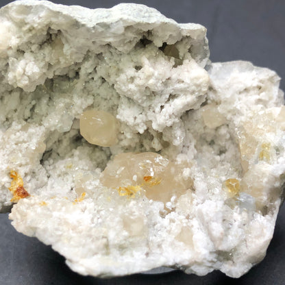 Close-up of the AUCTION- Geode with Calcite from Worthington, Ohio, USA by The Crystalary, featuring a rough gray exterior and open to display clear crystals with hints of honey calcite inside.