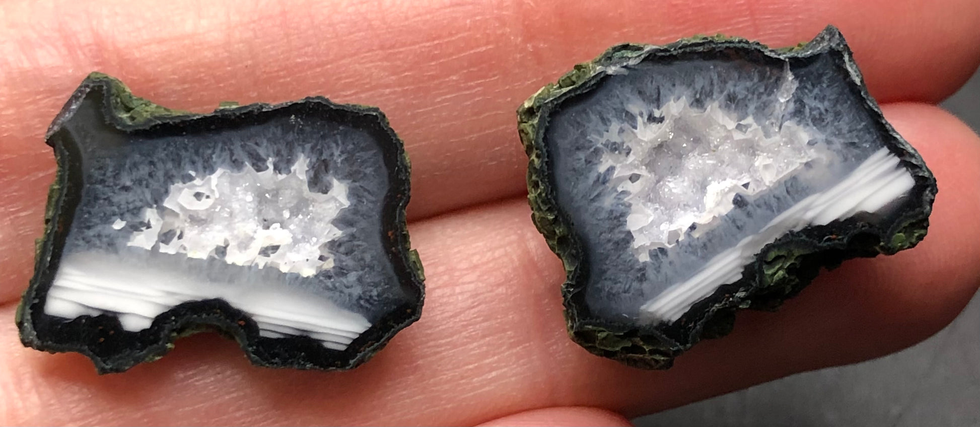 A close-up of a Tabasco geode from The Crystalary, originating in Tabasco, Mexico, rests on a person's fingertips. Its dark outer layer and crystal-filled interior make for a stunning contrast between the white druzy quartz crystals and the dark edges.