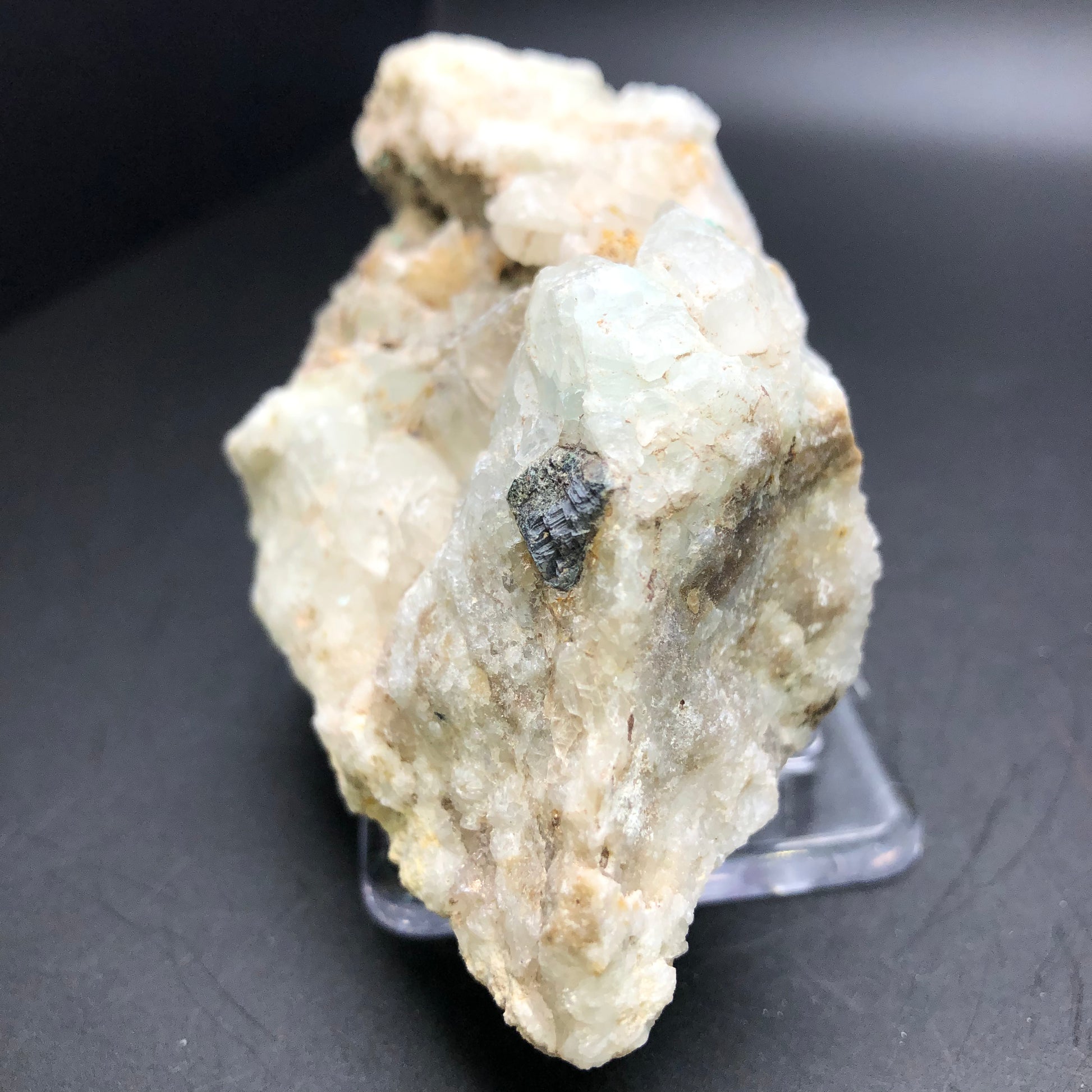 Introducing the AUCTION- Calcite, Quartz from The Crystalary: This stunning natural mineral specimen displays an exquisite druzy white quartz with delicate, translucent surfaces, complemented by a dark crystal embedded within. It is elegantly showcased on a clear stand against a plain black backdrop.