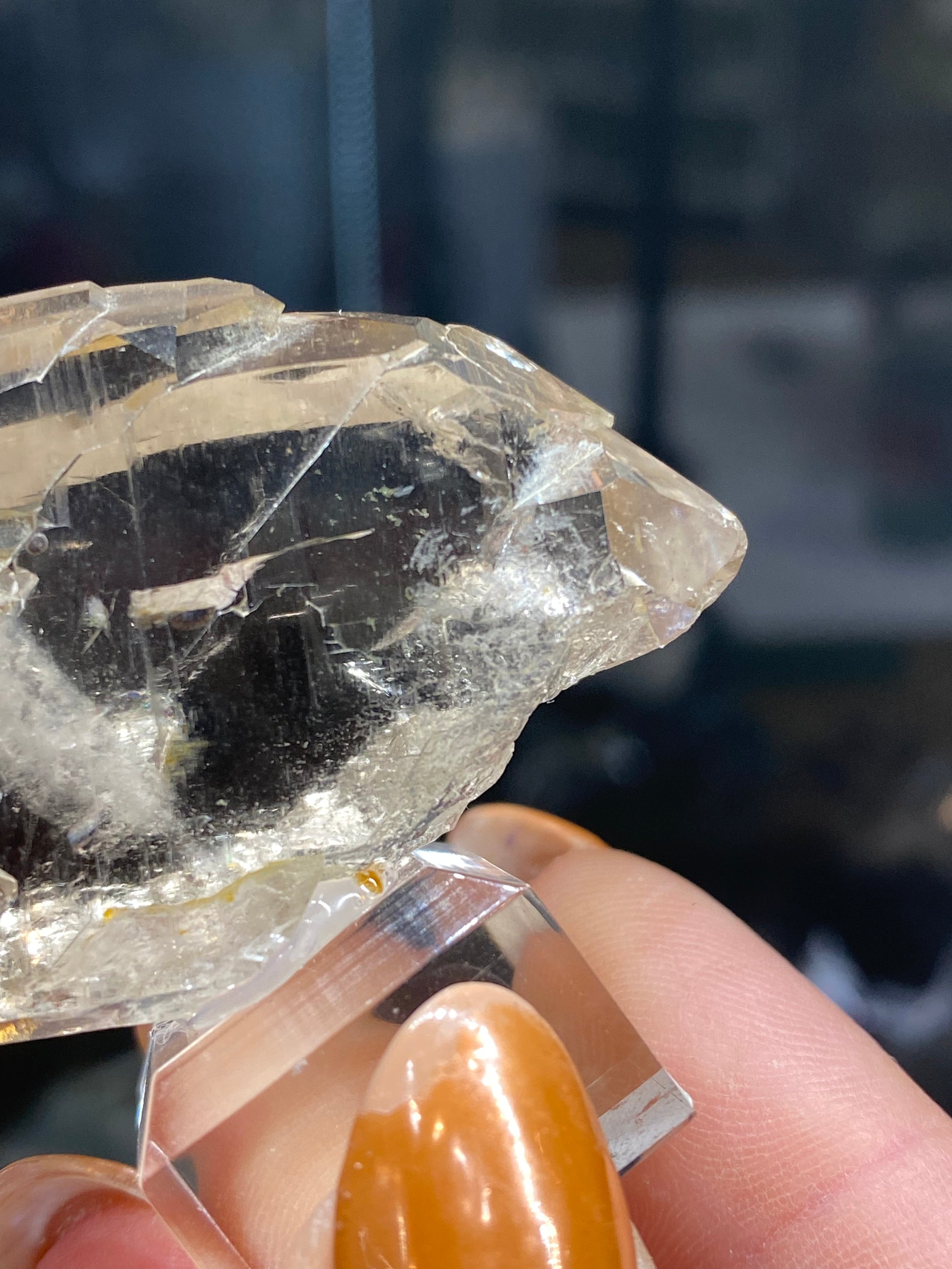 Close-up of a hand holding The Crystalary's Quartz, var. Faden- Mont Blanc Massif northwest flank, Auvergne-Rhône-Alpes, France (sku3008), showcasing its large size and multiple facets with a slightly cloudy appearance reminiscent of genuine faden quartz. The background is blurred, drawing attention to the intricate details of this stunning mineral piece, evoking the magnificent landscapes of the Mont Blanc Massif.