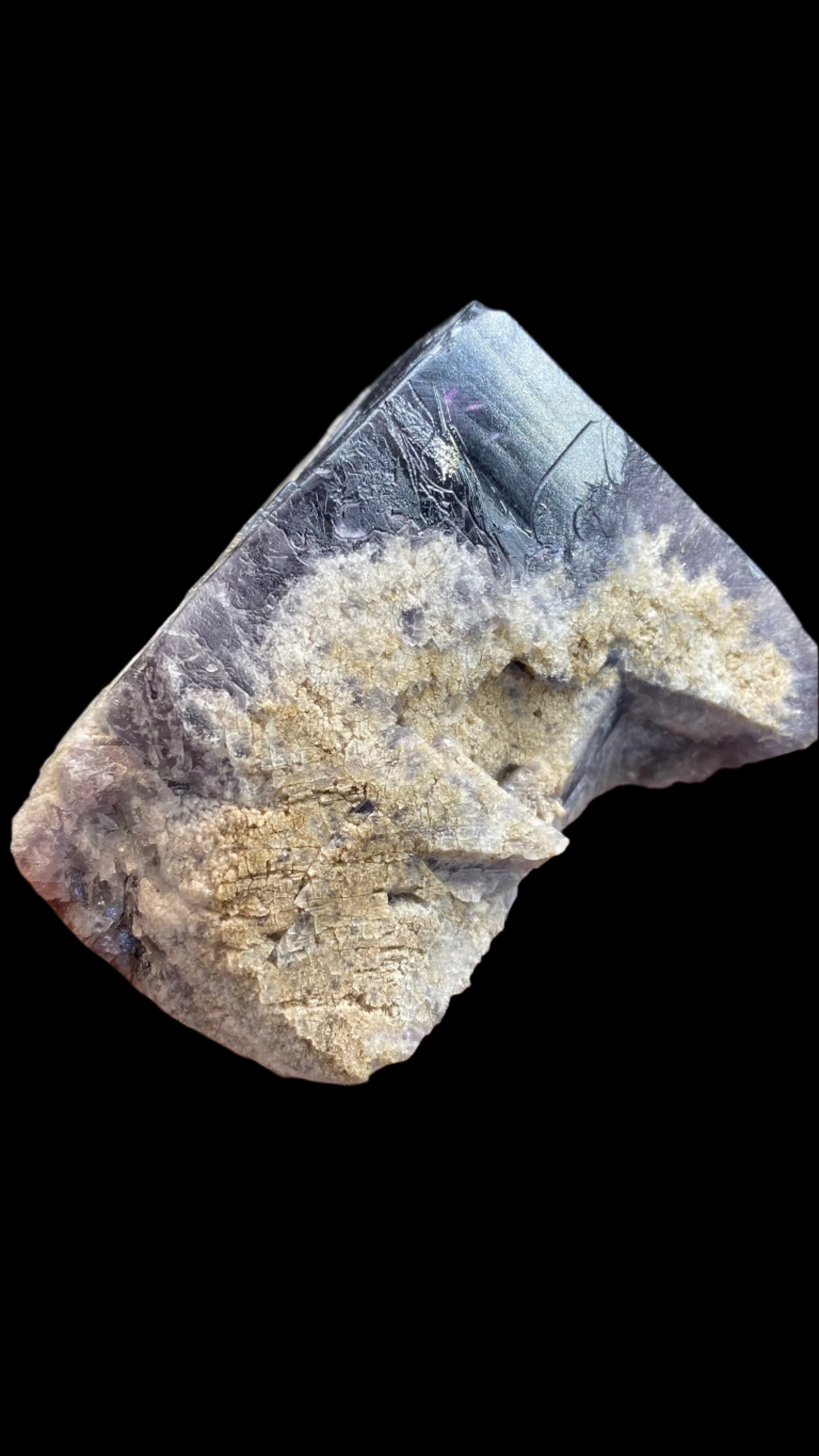 A hand holding a rough Fluorite specimen from The Crystalary's collection, originating from the Purple Rain Pocket in the Lady Annabella Mine, Eastgate, Weardale, Co. Durham, England (sku 3020). This piece showcases dark, shiny metallic-like surfaces complemented by beige crystalline formations, with an intriguing texture and structure reflective of its distinctive origin.