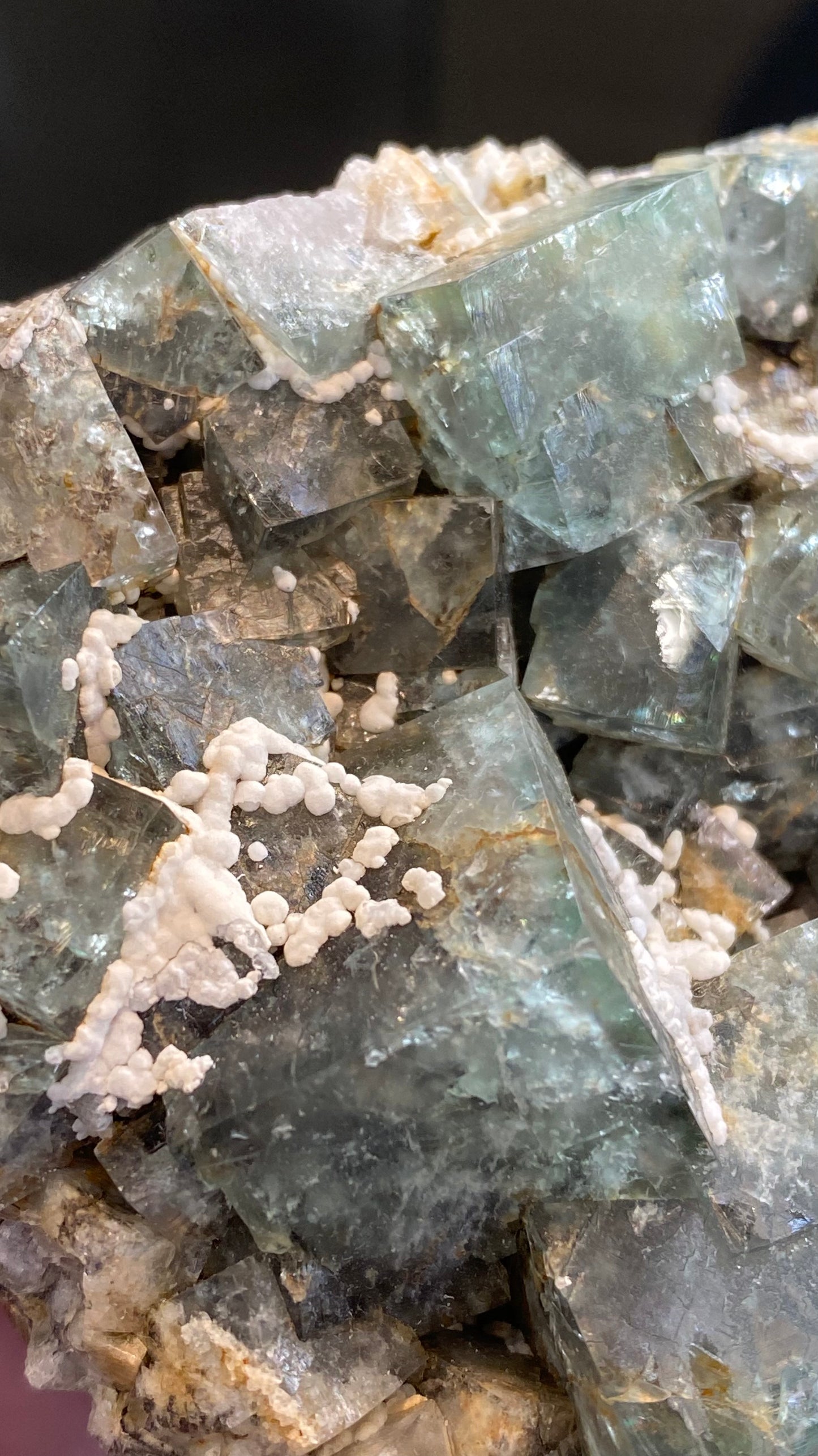 Image focused on a cluster of greenish translucent fluorite crystals with cubic formations from the Fairy Holes Pocket, Lady Annabella Mine. The surface features scattered white mineral deposits intertwining with calcite and geometric shapes, creating a striking texture and color contrast. Available from The Crystalary under SKU 3021.