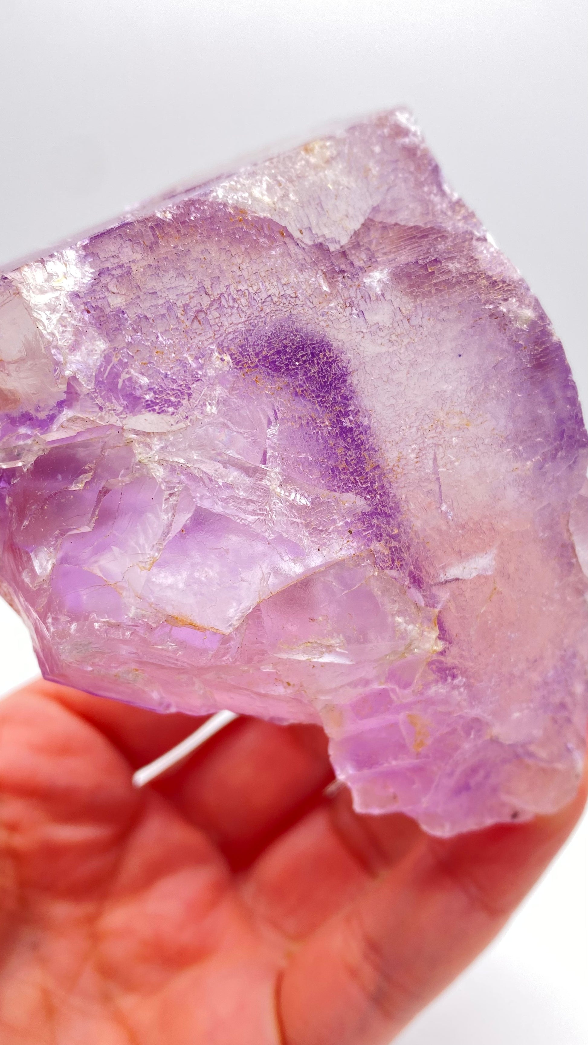 Close-up of a hand holding a striking Fluorite crystal from Lead Hill, Cave-In-Rock, Hardin County, Illinois, USA by The Crystalary. This large, translucent purple specimen features jagged edges and showcases various shades of purple with some areas more transparent and others opaque. The background is out of focus.