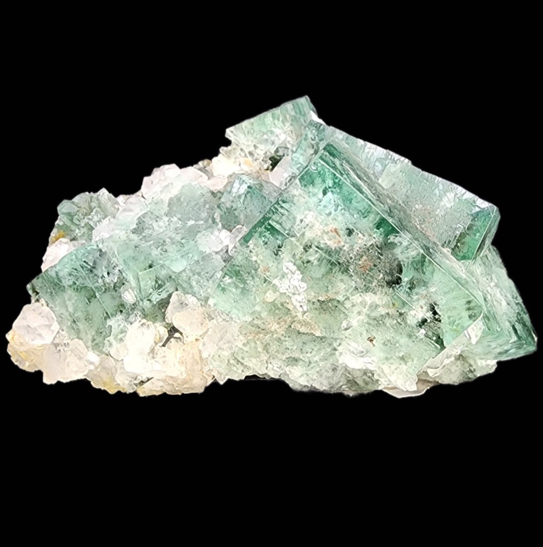 The Crystalary presents the Fluorite - Supernova Pocket from Diana Marie Mine, Weardale, Co. Durham, England: An unpolished raw cluster of green fluorite crystals displaying a natural blend of translucent green and white shades set against a solid black background. The sharp surfaces highlight its natural geometric formations and edges, reminiscent of treasures from a supernova pocket.