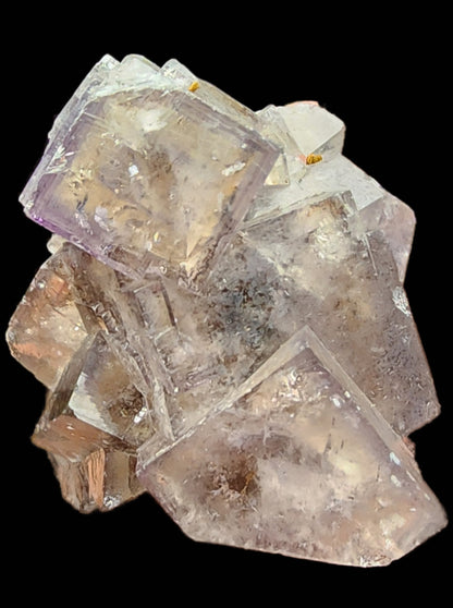 A glassy cluster of translucent, purple-hued fluorite crystals from The Crystalary's Fluorite collection—specifically sourced from the Cromwell Pocket in Greenlaws Mine, Daddry Shield, Stanhope, Co. Durham, England—exhibits a cubic structure with some internal fractures and surface imperfections. The crystals display subtle color changes and are set against a black background.